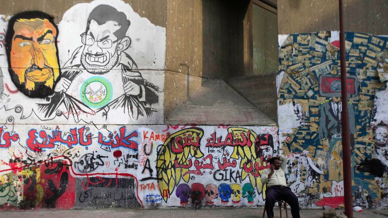 A man sits in front of graffiti denouncing ousted President Mursi with members of Brotherhood's during the Egyptian uprising along Mohamed Mahmoud Street near Tahrir Square in Cairo
