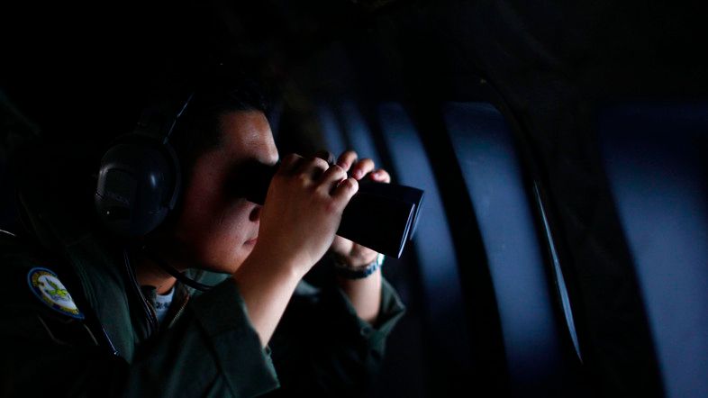 A crew member from the Royal Malaysian Air Force uses binoculars onboard a Malaysian Air Force CN235 aircraft during a Search and Rescue (SAR) operation to find the missing Malaysia Airlines flight MH370, in the Straits of Malacca