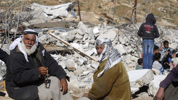 Palestinians sit in front of the remains of their house after it was demolished by the Israeli army south of the West Bank city of Hebron