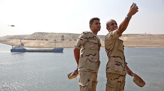Egyptian soldier take a "selfie" photo on a smartphone as a vessel makes its way through a section of the New Suez Canal, operated by the Suez Canal Authority, in Ismailia, Egypt, on Wednesday, Aug. 5, 2015. The expansion will meet future demand, with traffic expected to double to 97 vessels a day by 2023, said Mohab Mameesh, head of the Suez Canal Authority. Photographer: Shawn Baldwin/Bloomberg via Getty Images