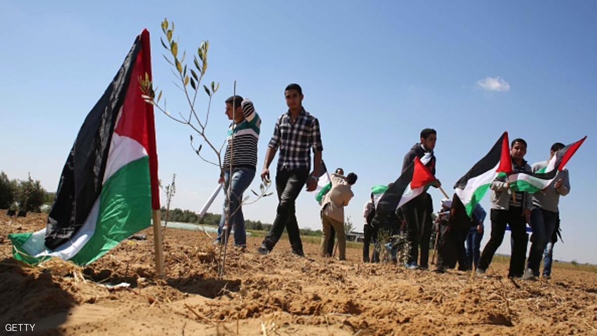 Palestinians hold their national flag as they plant olive trees to mark Land Day during a symbolic ceremony held in the village of Abassan, east of Khan Yunis near the border fence between Israel and the southern Gaza Strip on March 31, 2015. On the annual Land Day, demonstrations are held to remember six Arab Israeli protesters who were shot dead by Israeli police and troops during mass protests in 1976 against plans to confiscate Arab land in the Galilee. AFP PHOTO / SAID KHATIB (Photo credit should read SAID KHATIB/AFP/Getty Images)