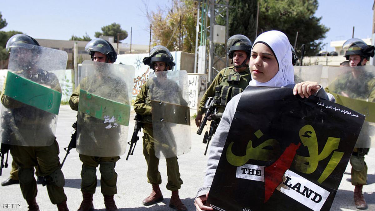 A Palestinian protester holds a poster for Land Day, which commemorates the deaths in 1976 of Arab Israelis during mass demonstrations against plans to confiscate Arab land in Galilee, as she stands in front of Israeli soldiers during a weekly demonstration against the Israeli separation barrier and the expansion of Jewish settlements, in the West Bank village of Maasarah, near Bethlehem, on March 29, 2013. Israel deployed significant security reinforcements in the occupied West Bank including east Jerusalem for demonstrations marking Land Day. AFP PHOTO/MUSA AL-SHAER (Photo credit should read MUSA AL-SHAER/AFP/Getty Images)